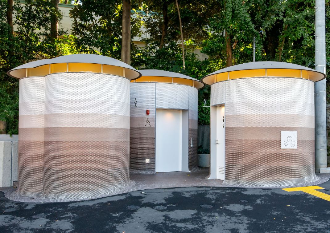 Des toilettes publiques circulaires modernes avec des murs à motifs et des toits arrondis, entourées de verdure.