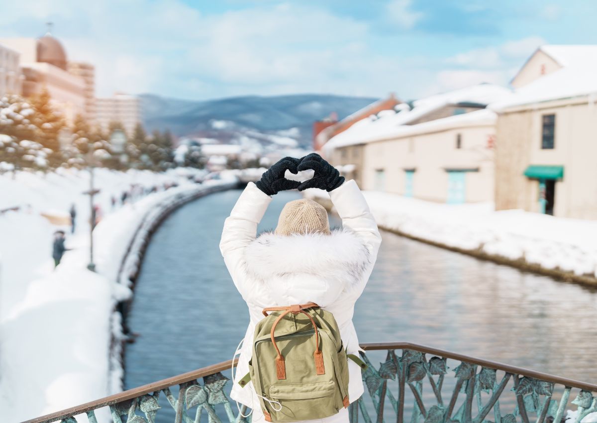 Voyageuse de dos formant un cœur avec les mains au-dessus de la tête dans les rues enneigées d’Otaru, Hokkaido, Japon