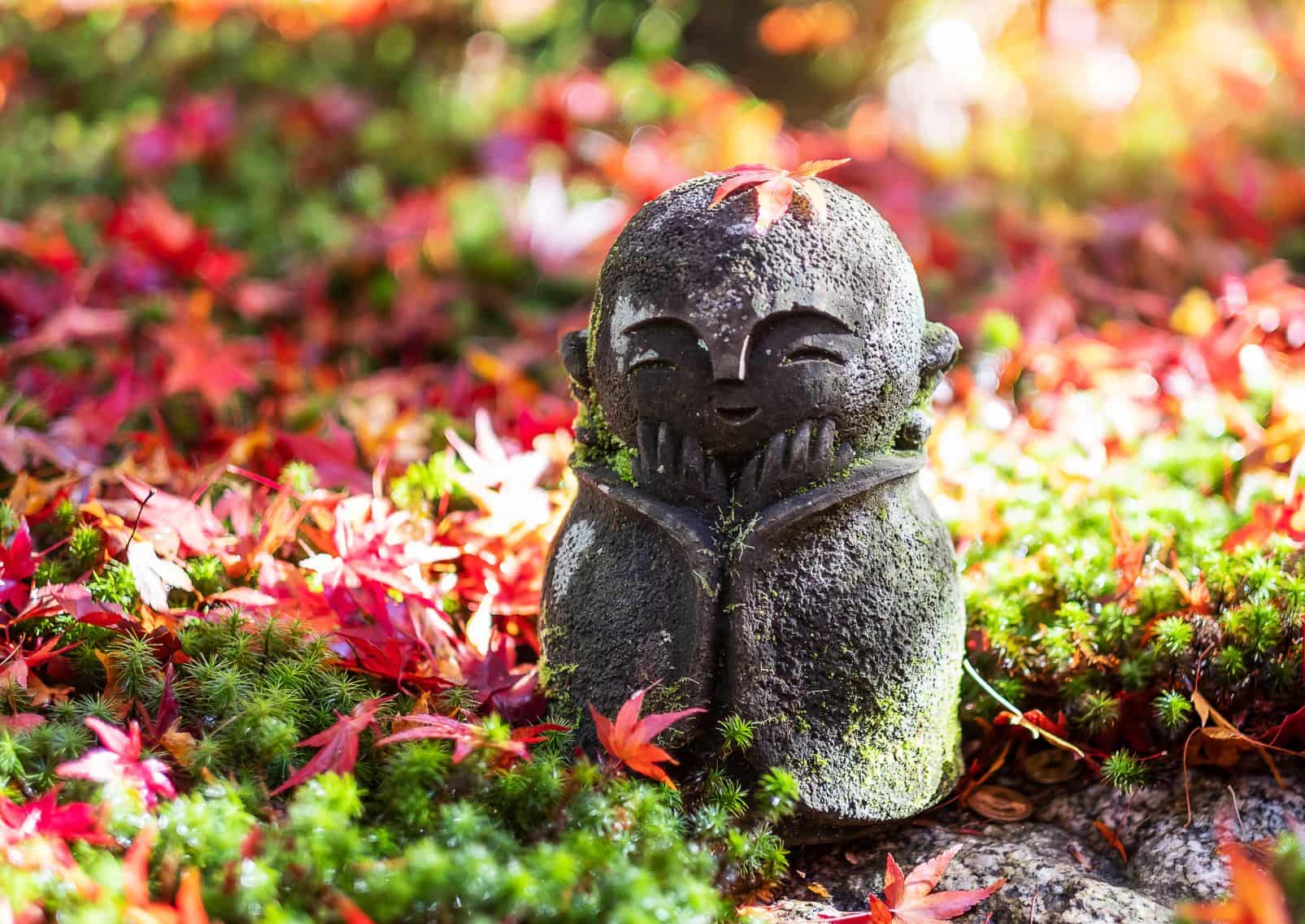 Poupée sculptée japonaise Jizo avec une feuille d'érable rouge tombante dans le jardin japonais du temple Enkoji, Kyoto, Japon 