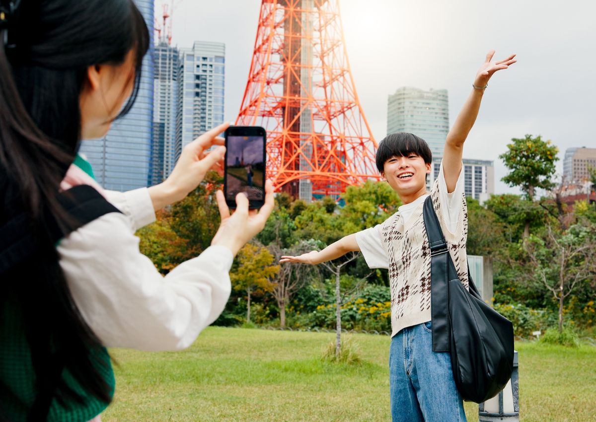 Jeune homme se faisant prendre en photo par une jeune femme devant la Tokyo Tour, Tokyo, Japon