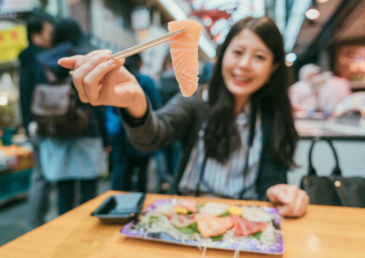Jeune femme dégustant des sushis au marché Kuromon, Osaka, Japon