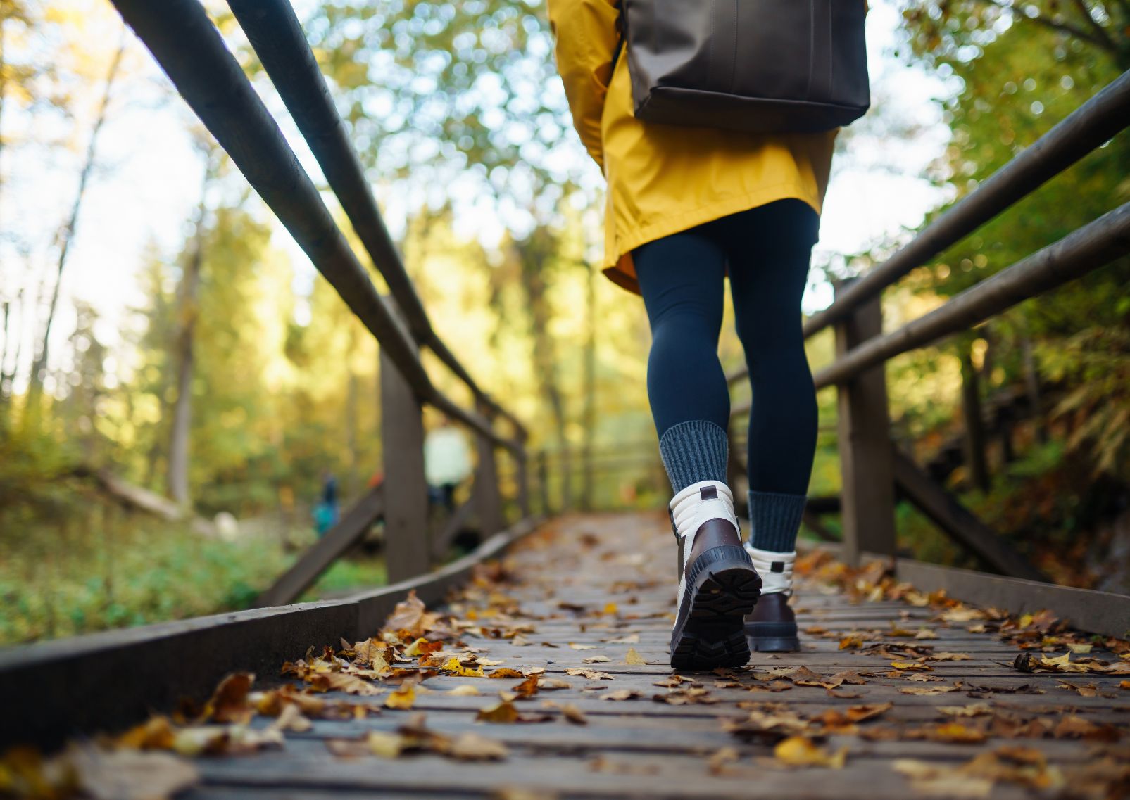 Bottes d’une femme marchant sur un chemin de randonnée en bois dans une forêt en automne.