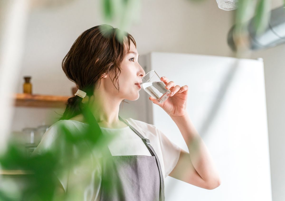 Jeune femme portant un tablier buvant de l'eau du robinet, Japon