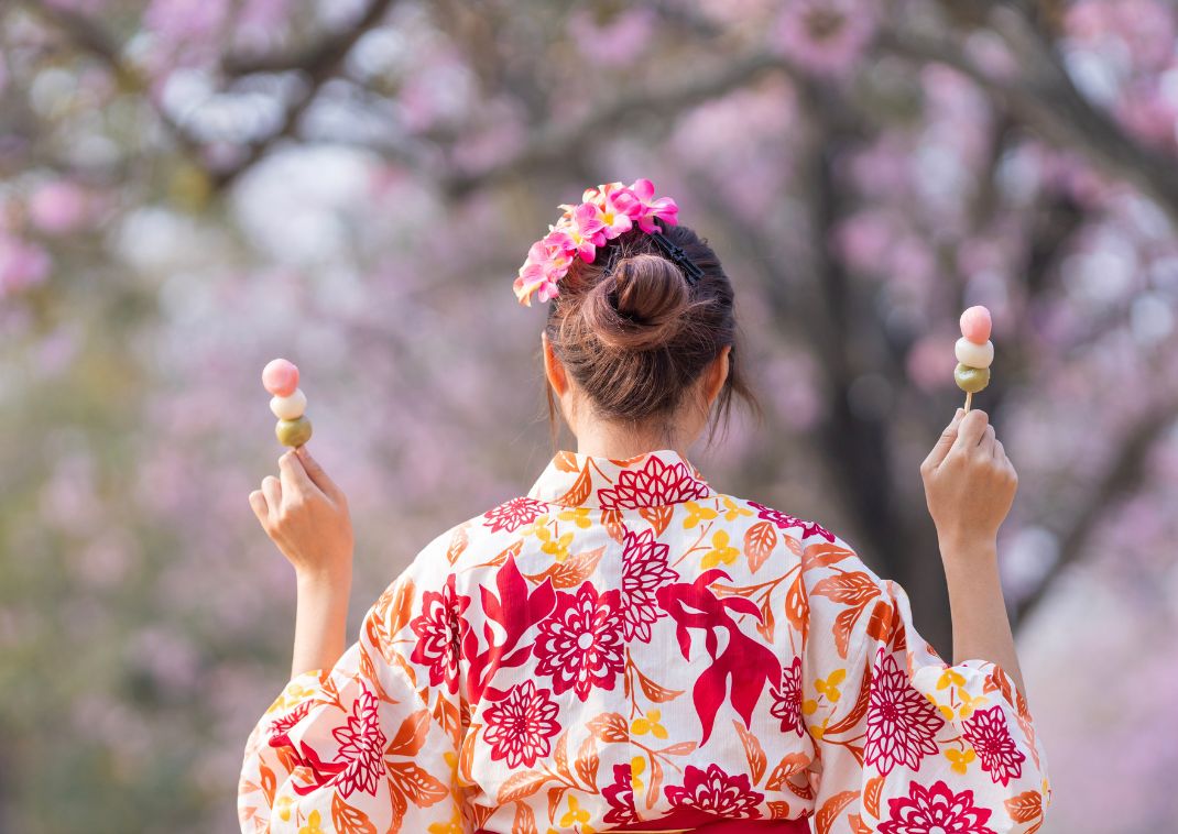 Femme en kimono de dos tenant deux brochettes de Hanami dango, des douceurs traditionnelle de saison au Japon