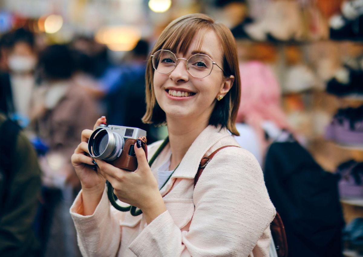 Jeune femme souriante, tenant un appareil photo dans une rue au Japon