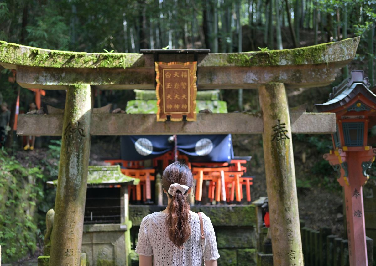 Jeune femme de dos se tenant devant un torii au sanctuaire Fushimi Inari, Kyoto, Japon
