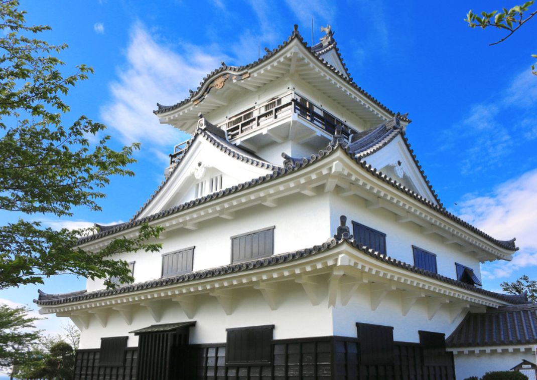 Château japonais traditionnel blanc de Chiba avec des toits noirs et des détails architecturaux en bois, sous un ciel bleu parsemé de nuages et entouré de verdure.