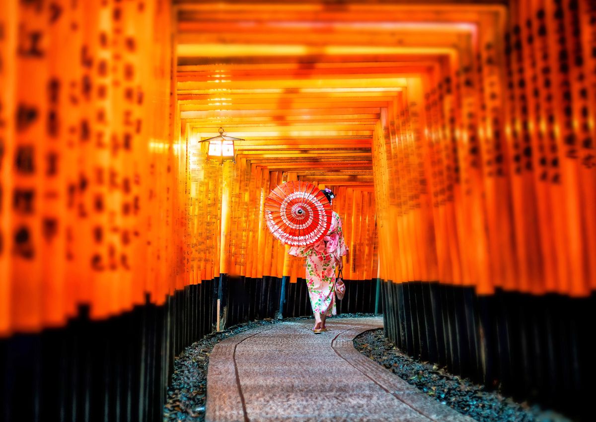 Jeune femme en kimono avec une ombrelle dans le tunnel de torii rouges du sanctuaire Fushimi Inari, Kyoto, Japon