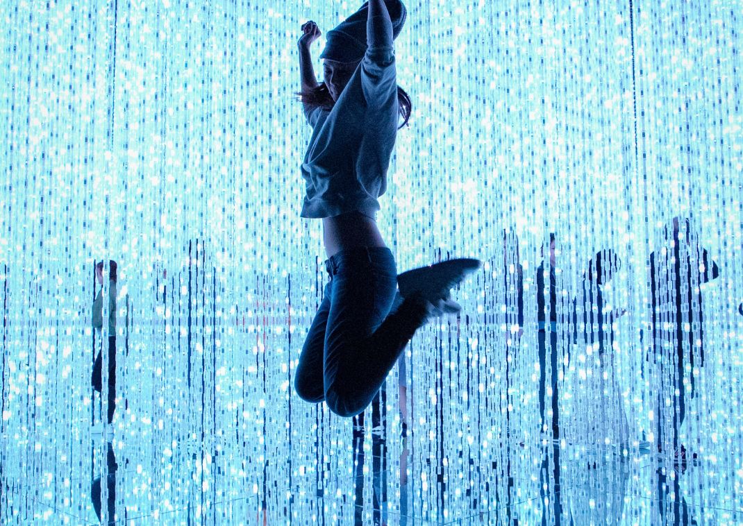 Femme sautant devant des guirlandes lumineuses au musée TeamLab de Tokyo, Japon