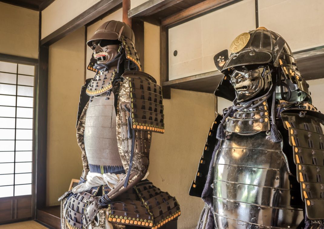 Deux armures de samouraï japonaises exposées dans une pièce traditionnelle, avec des murs en bois et des portes coulissantes en papier shoji.
