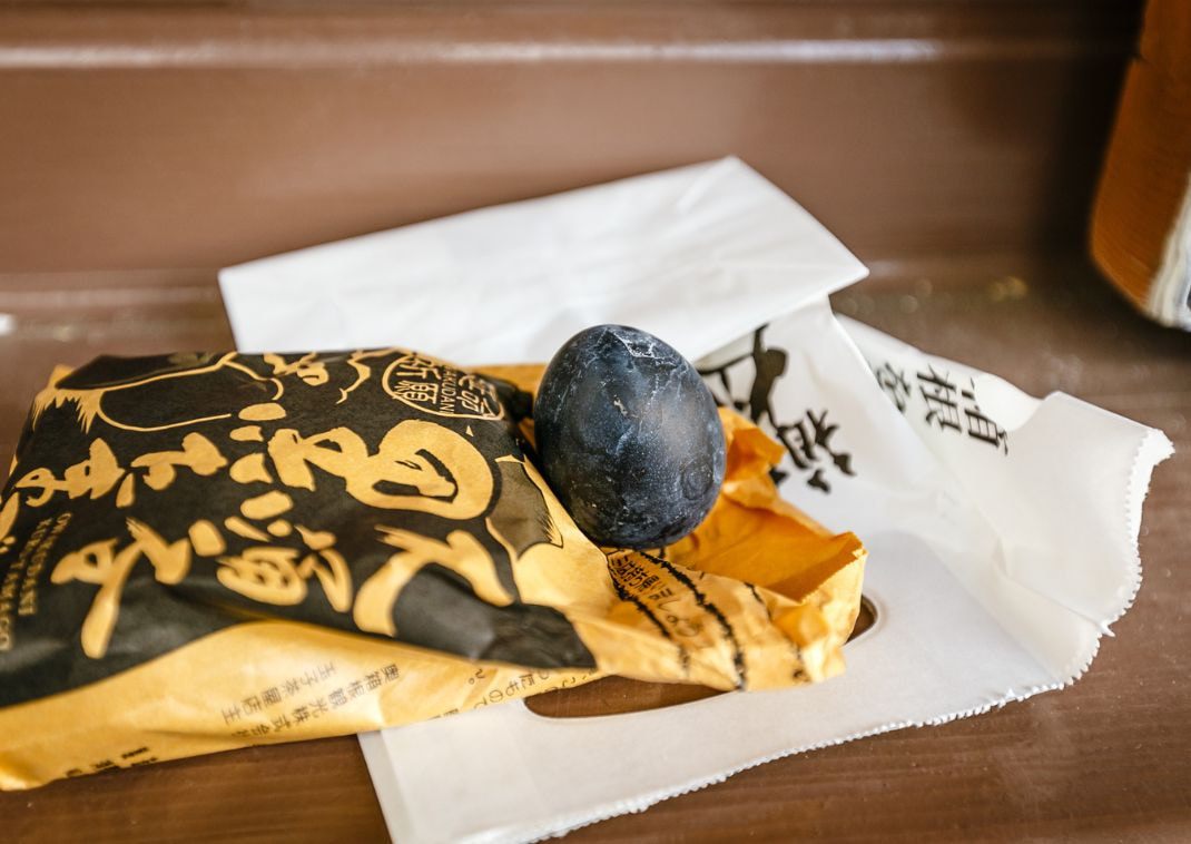 Œuf noir de Hakone, spécialité locale, posé sur son emballage en papier jaune et noir, sur une table en bois.