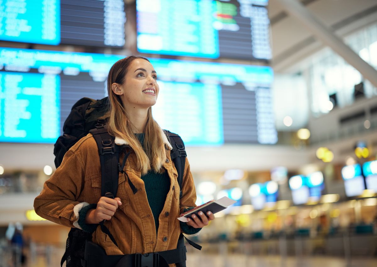 Jeune femme avec un sac à dos dans un aéroport, tenant ses documents de voyage à la main.