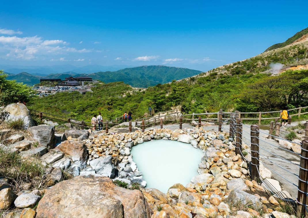 Bassin d’eau thermale laiteuse et fumante entouré de rochers et de barrières en bois, dans la vallée volcanique d’Owakudani à Hakone.