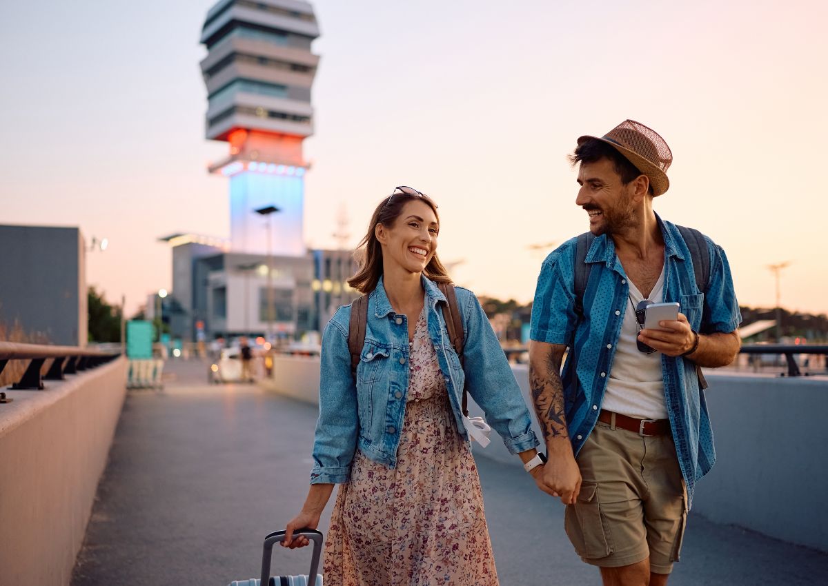 Couple se tenant la main et marchant devant un aéroport au coucher du soleil