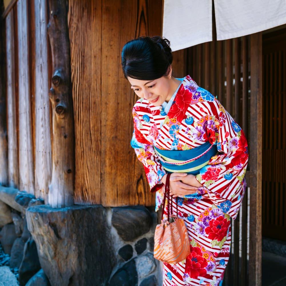 Femme japonaise en kimono coloré s'inclinant devant un bâtiment traditionnel en bois à Kyoto