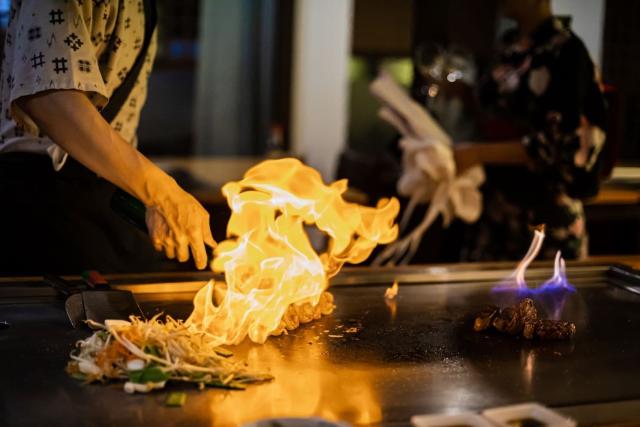 Chef préparant un repas teppanyaki avec du bœuf et des légumes grillés