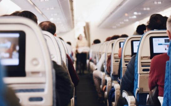 Intérieur d'un grand avion de passagers avec des personnes assises et une hôtesse de l'air en uniforme marchant dans l'allée.