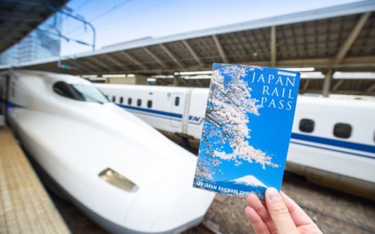 Main tenant un billet de Japan Rail Pass devant un Shinkansen à la gare de Tokyo.
