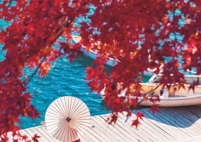 Femme portant une robe rouge et ombrelle blanche au bord de l’eau durant l’automne japonais