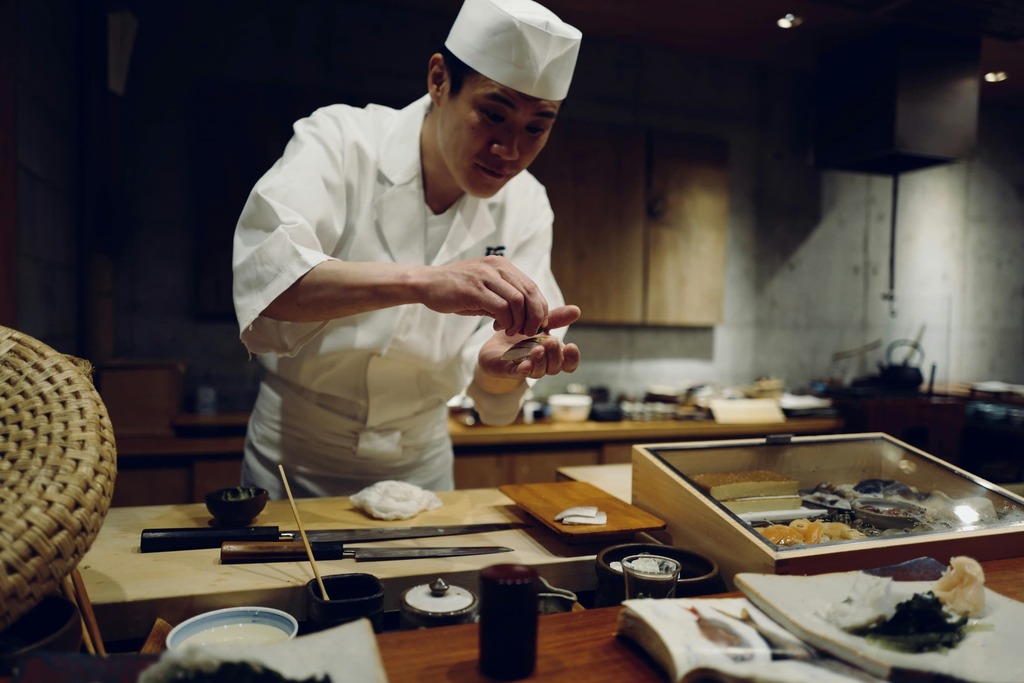 Un chef japonais prépare des sashimis devant le comptoir d'un restaurant japonais de sushis.