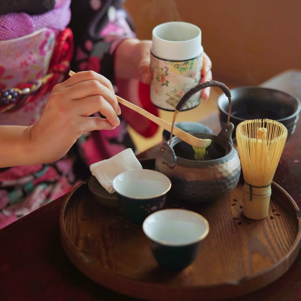 Femme japonaise préparant du thé matcha lors d'une cérémonie traditionnelle du thé à la maison, avec de la poudre de matcha, des herbes et une théière.