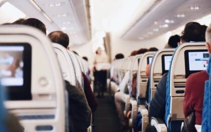 Intérieur d'un grand avion de passagers avec des personnes assises et une hôtesse de l'air en uniforme marchant dans l'allée.