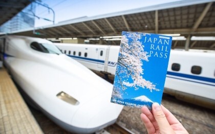 Main tenant un billet de Japan Rail Pass devant un Shinkansen à la gare de Tokyo.