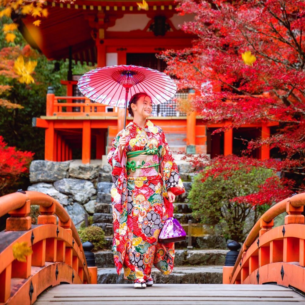 Jeune femme en kimono sur un pont rouge dans un temple en automne, Japon