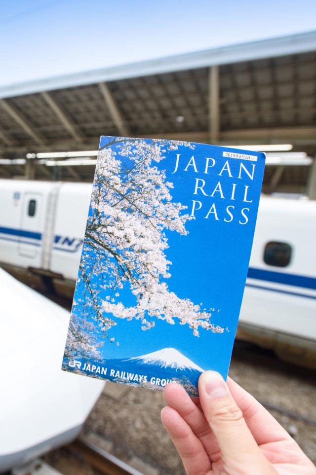 Main tenant un billet de Japan Rail Pass devant un Shinkansen à la gare de Tokyo.